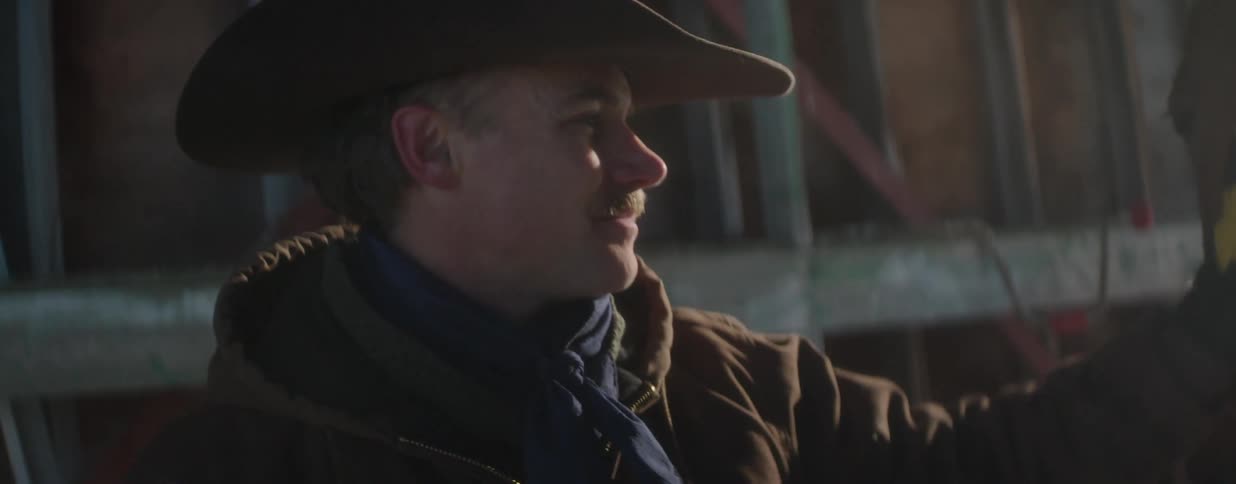 Close-up of a cowboy in a hat sharing a tender moment with his horse in a softly lit barn