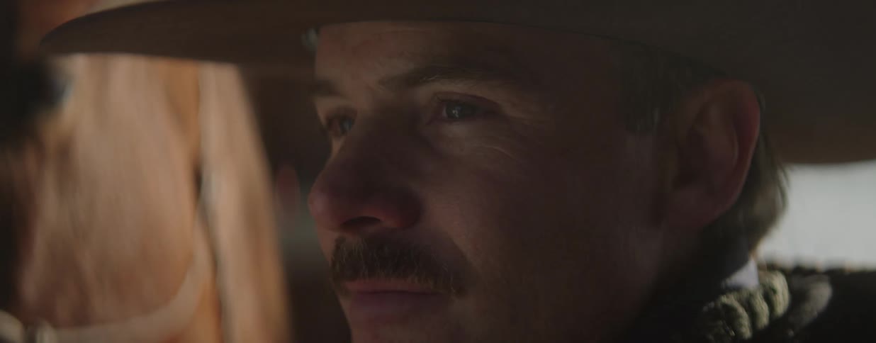 A moody close-up profile shot of a thoughtful cowboy with a mustache wearing a hat