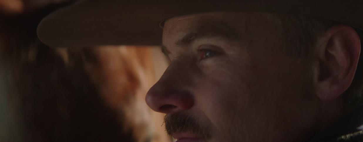 A cowboy shares a quiet, tender moment with his horse, gently stroking its face in a dimly lit stable