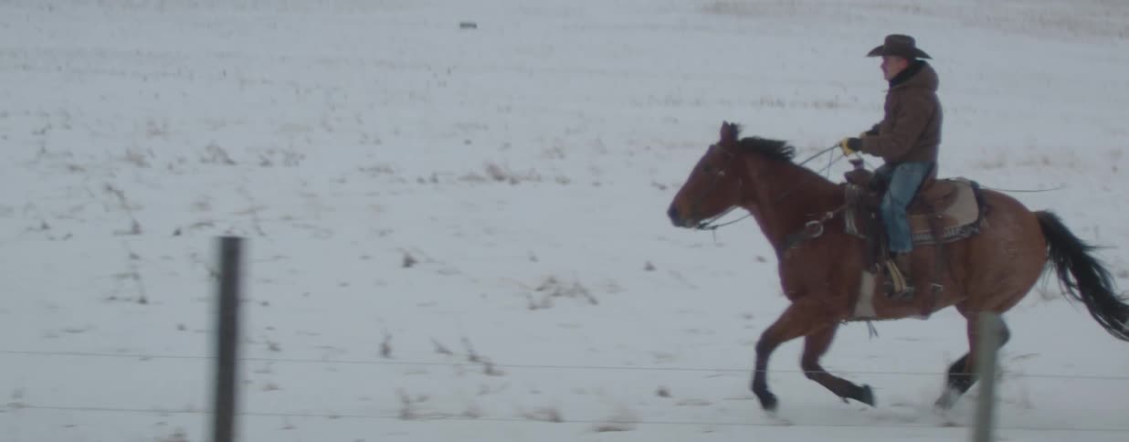 A cowboy gallops on his horse through a snowy winter landscape in slow motion