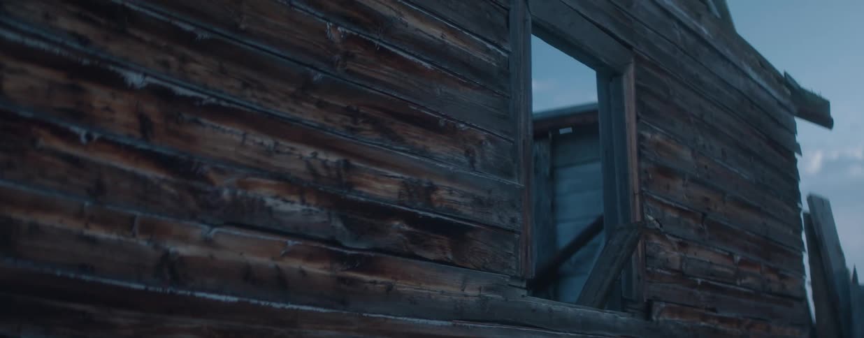 A slow, eerie zoom-out from the weathered wooden wall of an abandoned, dilapidated building at dusk