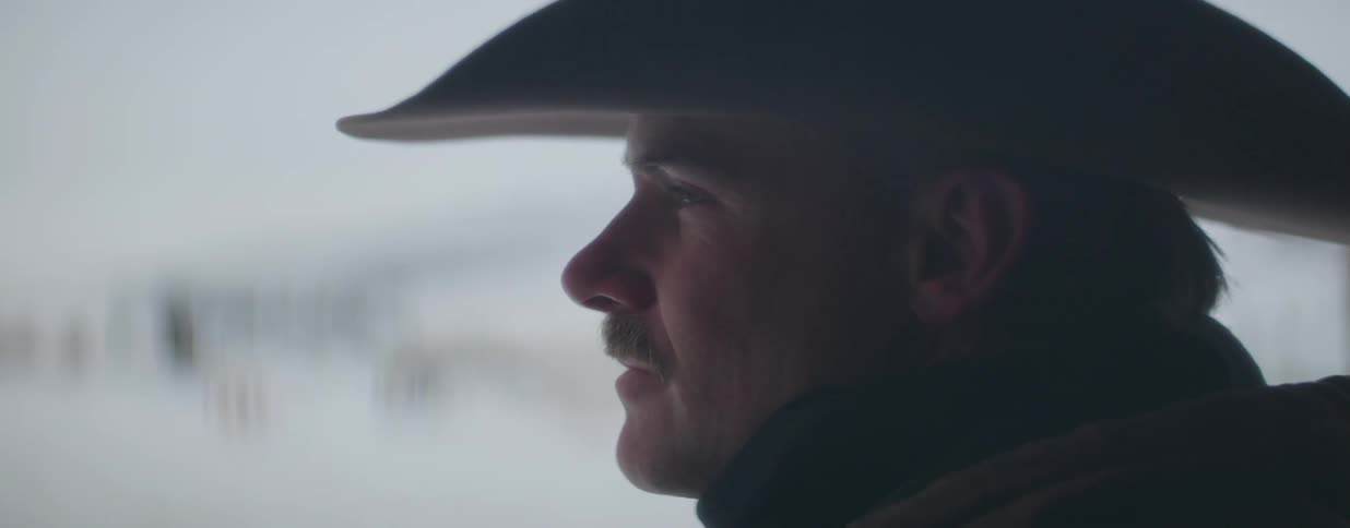 A slow rack focus on the profile of a cowboy looking out over a snowy winter landscape