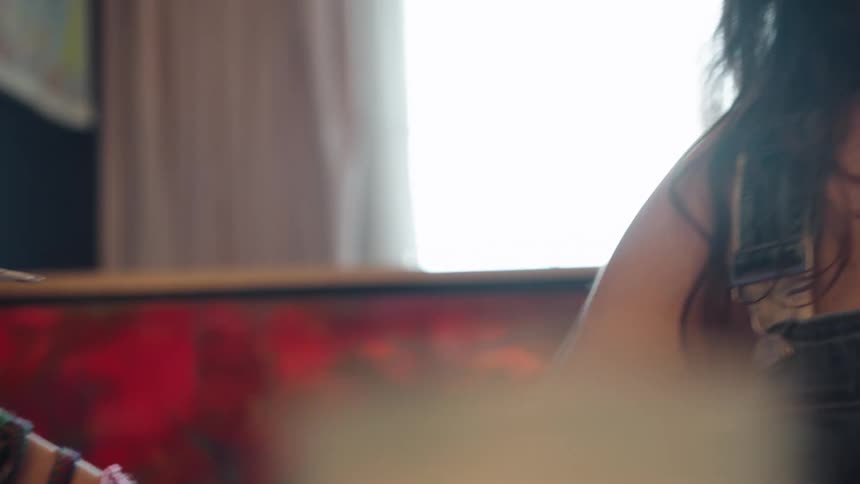 Close-up of a young artist's hand gracefully applying paint to a canvas, slowly revealing her concentrated expression in a sunlit room