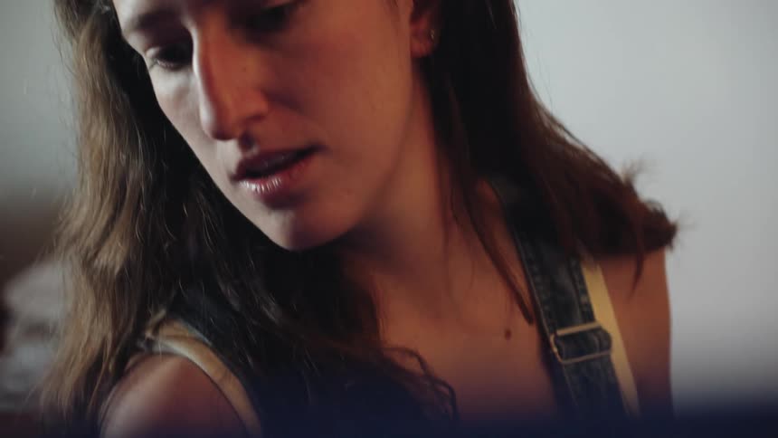 A close-up slow-motion shot pans from an artist's hand holding a paintbrush to her concentrated face as she works