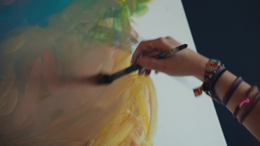 Close-up of an artist's hand applying vibrant, colorful brushstrokes to create an abstract painting on a canvas