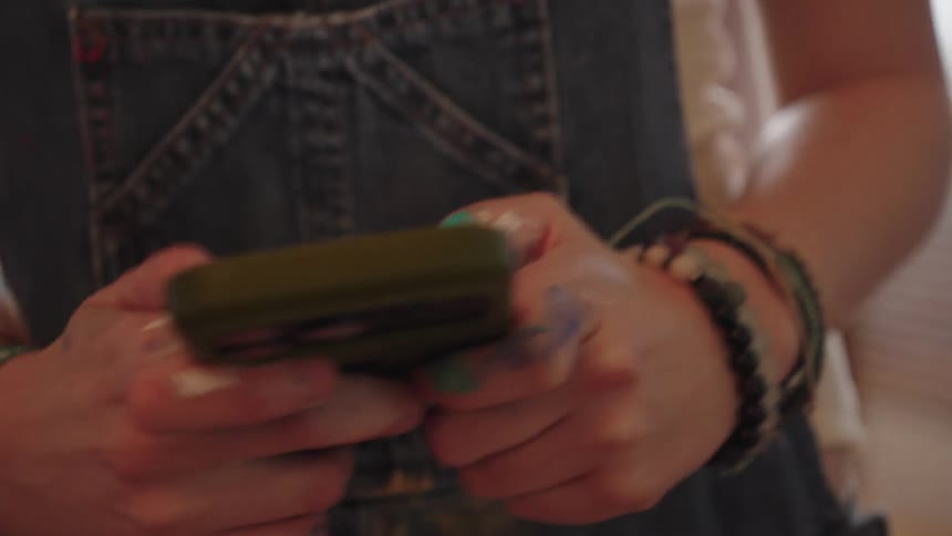 A close-up of an artist's paint-covered hands as they scroll on a smartphone while taking a break in their studio