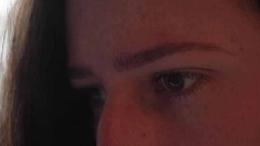 Extreme close-up of a young woman's focused eye as light reflects in her pupil while she looks down