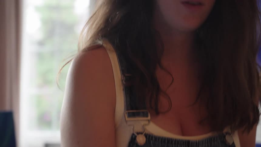 A young female artist in overalls concentrates deeply on her work as she paints in slow motion in a naturally lit studio