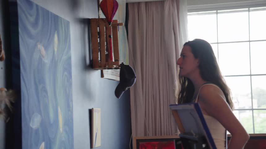 A creative female artist carefully hangs her large, abstract blue painting on the wall in slow motion