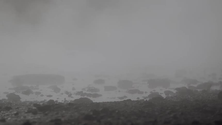 Heavy steam rises from a rocky, wet ground in a mysterious and desolate landscape
