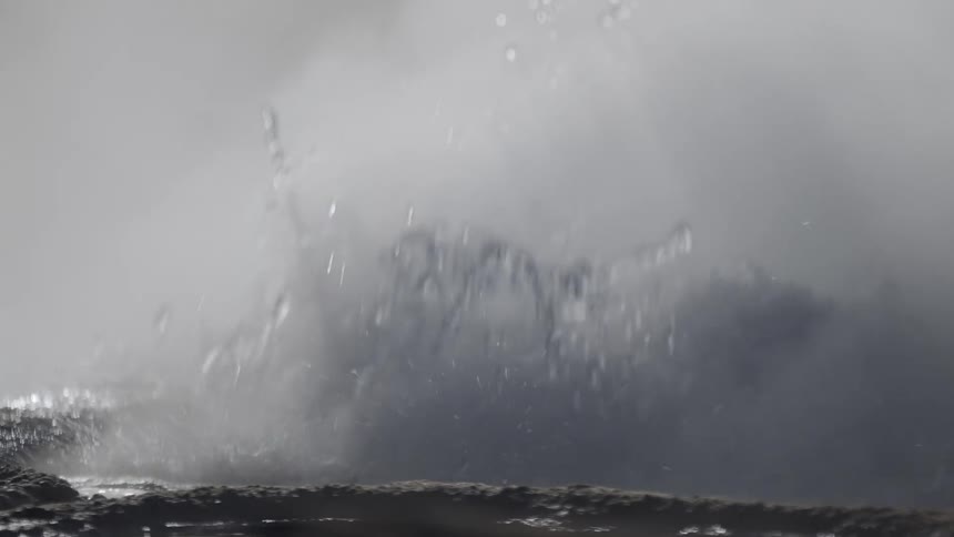 A super slow-motion close-up captures the violent eruption of a geyser, with boiling water splashing and steam rising from the ground
