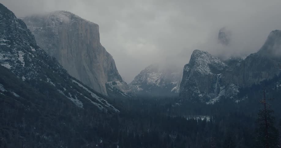 A majestic view of the snow-dusted Yosemite Valley reveals itself through the thick fog on a moody, overcast day