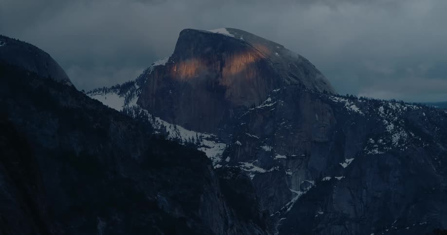The face of Half Dome in Yosemite is illuminated with two spots of golden light that look like eyes at sunrise