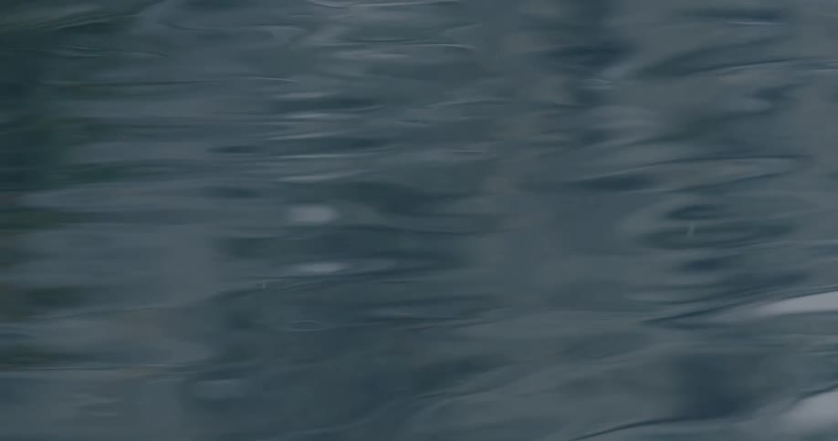 A moody and serene close-up of dark water rippling softly as light rain falls