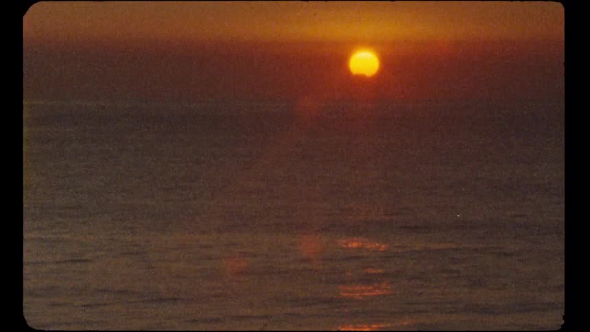 A vintage, grainy shot of a golden sun setting over the calm, endless ocean