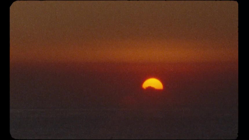 An authentic vintage Super 8mm film captures the glowing orange sun setting behind a hazy horizon
