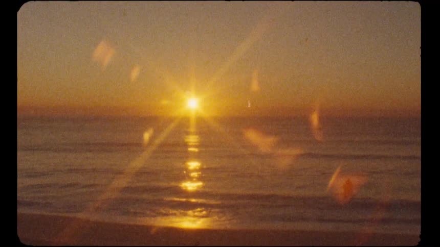 Nostalgic super 8 film look of a bright sunset over the ocean with two people wading in the water