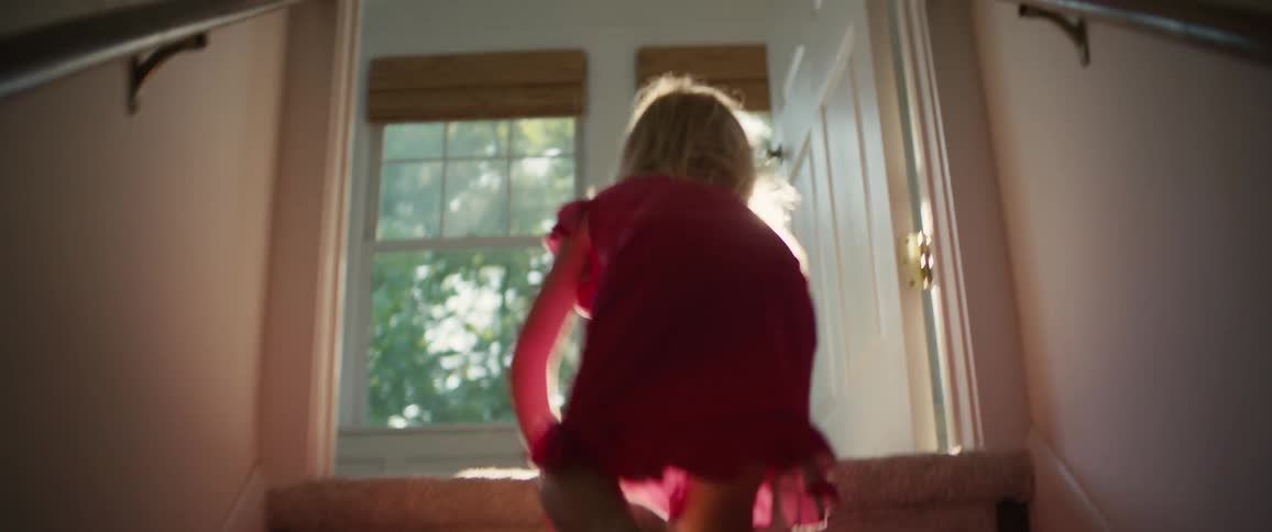 A joyful toddler girl crawls up the sunlit stairs at home and smiles happily at the camera