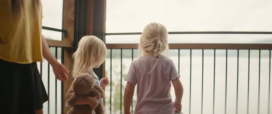 A mother joins her two young daughters on a balcony to enjoy the tranquil view of a large lake