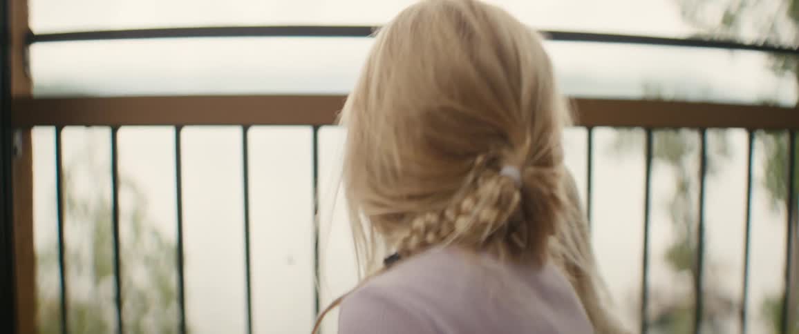 Two blonde sisters on a balcony overlooking a lake as the focus shifts to a tiny spider hanging from its web