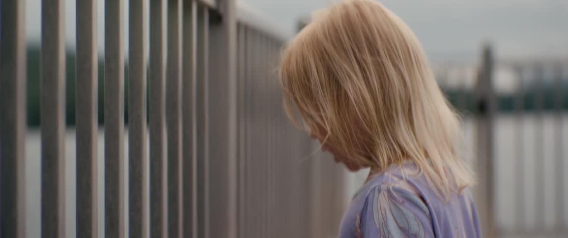 A little blonde girl runs along a boardwalk by the water with her arms outstretched