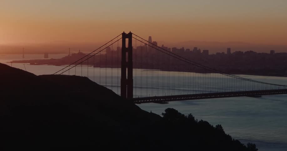 A static shot shows the Golden Gate Bridge silhouetted against a beautiful sunrise with the San Francisco skyline in the background