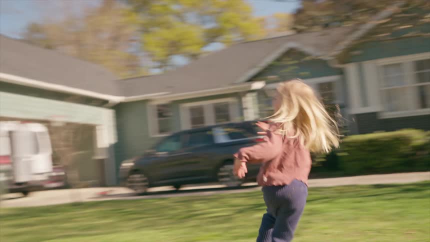 A joyful little blonde girl smiles and runs through a sunlit park in an energetic slow-motion shot