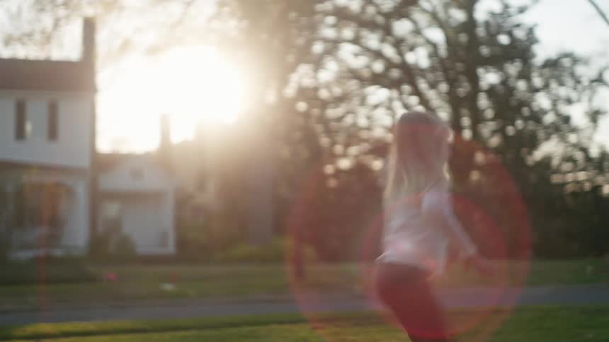 Two happy young sisters run barefoot through the grass in their front yard during a beautiful golden hour