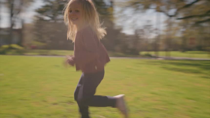 Carefree little girl with blonde hair running joyfully through a suburban park