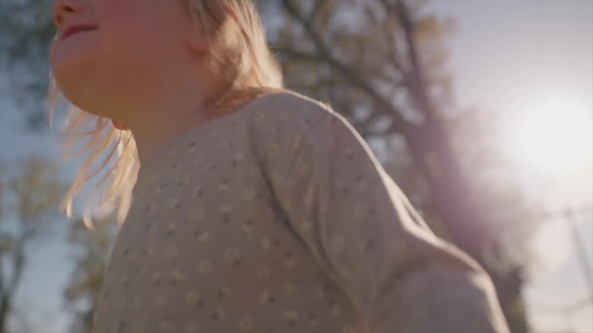 Backlit by the warm afternoon sun, a cute toddler smiles and plays with her yellow bucket on a quiet neighborhood sidewalk