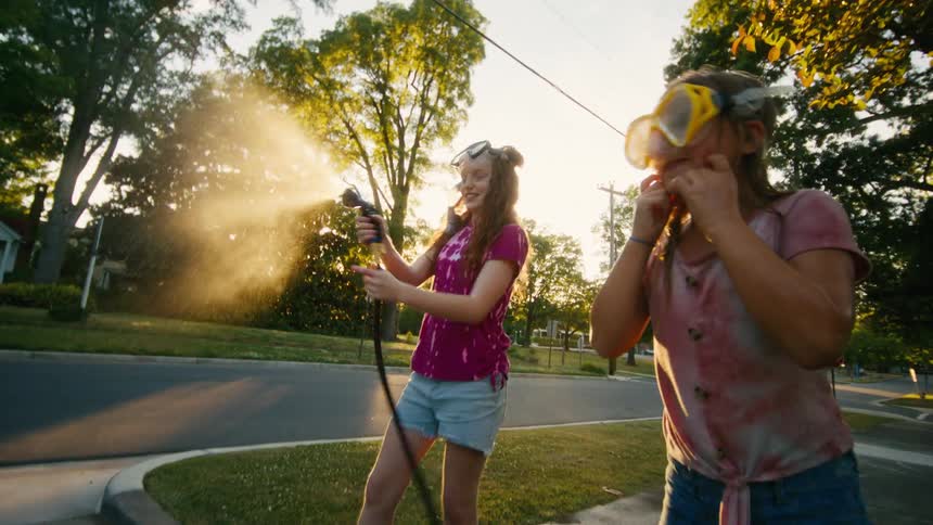 Playful kids in snorkel masks have a fun water hose fight on a suburban sidewalk at golden hour