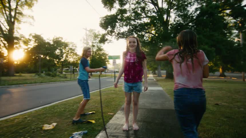 Joyful kids have a fight with a garden hose on a suburban sidewalk as the golden hour sun sets