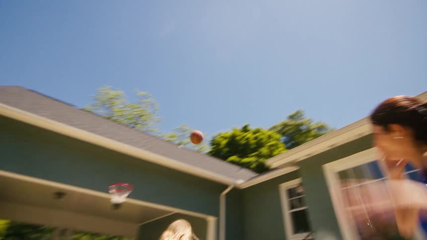 A mother and son play basketball in their driveway on a sunny day, and she scores a basket