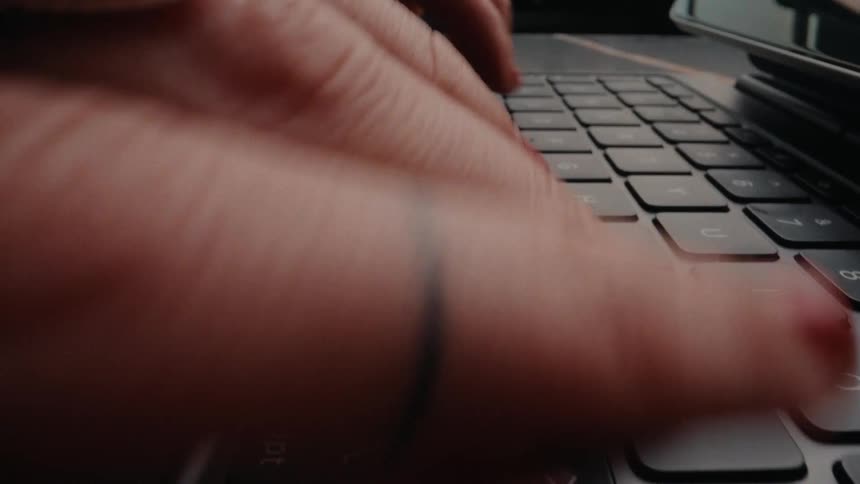 A woman's hands with red nail polish and rings open a laptop and begin typing quickly in a dramatic macro close-up shot