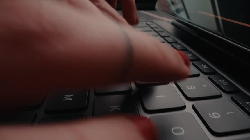 A close-up tracking shot of a woman with red nails opening a laptop and typing on the keyboard