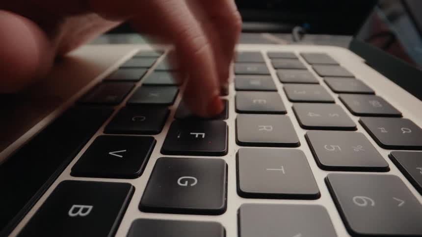 A hyperlapse close-up shot of frantic fingers typing rapidly on a modern laptop keyboard