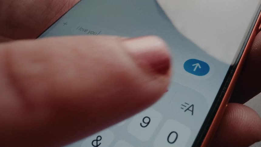 A close-up macro shot of a person typing and sending an 'I love you' message on a smartphone