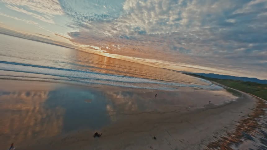 An exhilarating FPV drone flight speeds along a coastal bluff trail and out over the ocean waves during a dramatic sunset