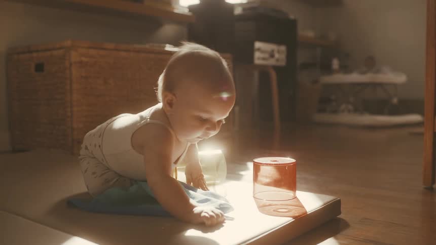 A cute baby sits on the floor bathed in warm sunlight and plays with toys in backlight