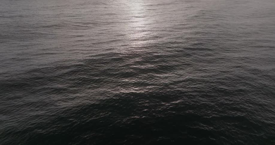 A tranquil and serene view of the dark, rippling ocean with a beautiful light reflection on the surface
