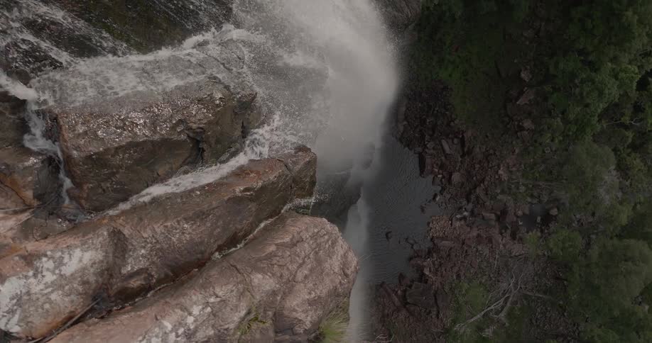 A top-down aerial perspective slowly pulls back to reveal the impressive drop of a waterfall crashing onto rocks below
