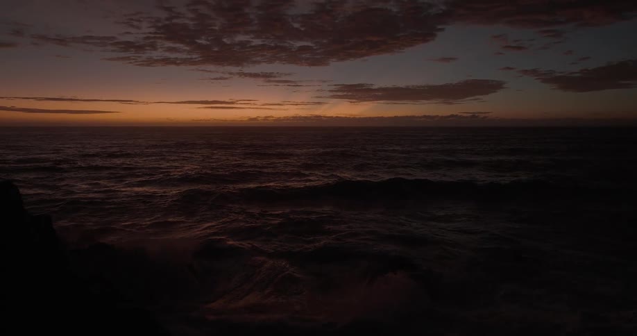 Powerful ocean waves crash in dramatic slow motion under a moody twilight sky