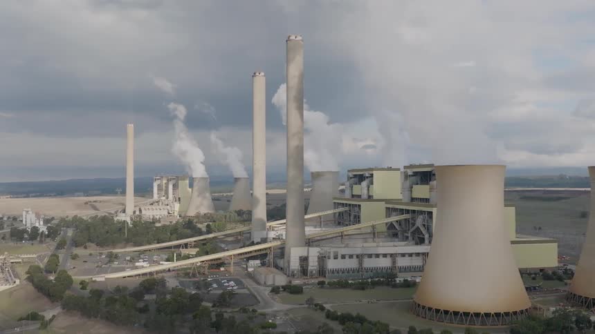 A slow aerial pan reveals a massive coal-fired power plant with steam and smoke rising into the overcast sky