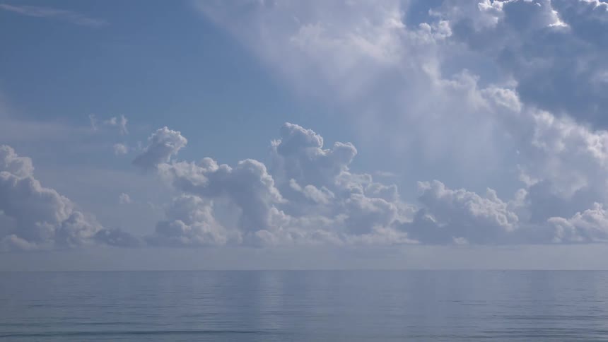 A serene time-lapse captures majestic white clouds moving and dissipating over the calm blue ocean