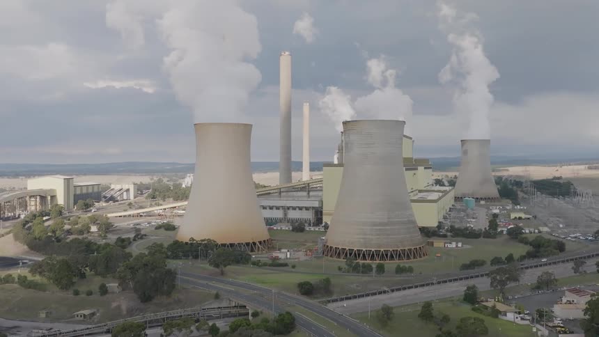 Aerial view of a large coal-fired power station with cooling towers and smokestacks releasing plumes of steam under a cloudy sky
