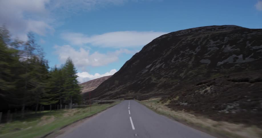 Driving along a winding country road through the mountainous Scottish Highlands on a beautiful day