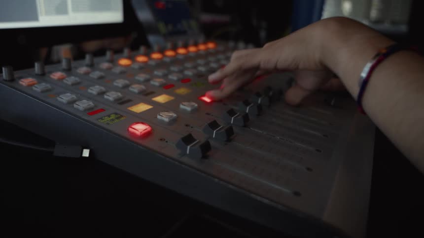 A sound engineer operates a professional audio mixing console in a dimly lit broadcast studio