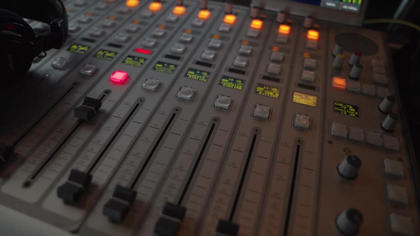A close-up slow zoom of a professional audio mixing board with blinking lights in a dimly lit radio studio