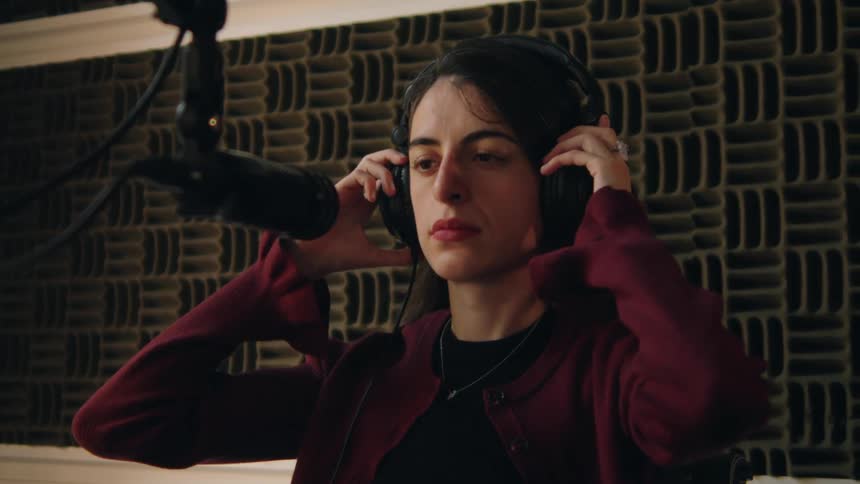 A focused young woman puts on her headphones in a professional soundproof recording studio