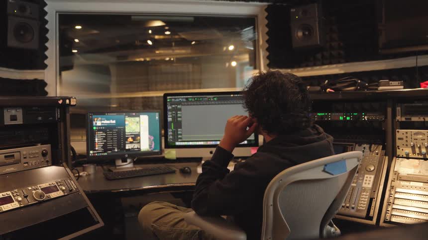A focused audio engineer sits at the mixing console in a professional recording studio, working on a project